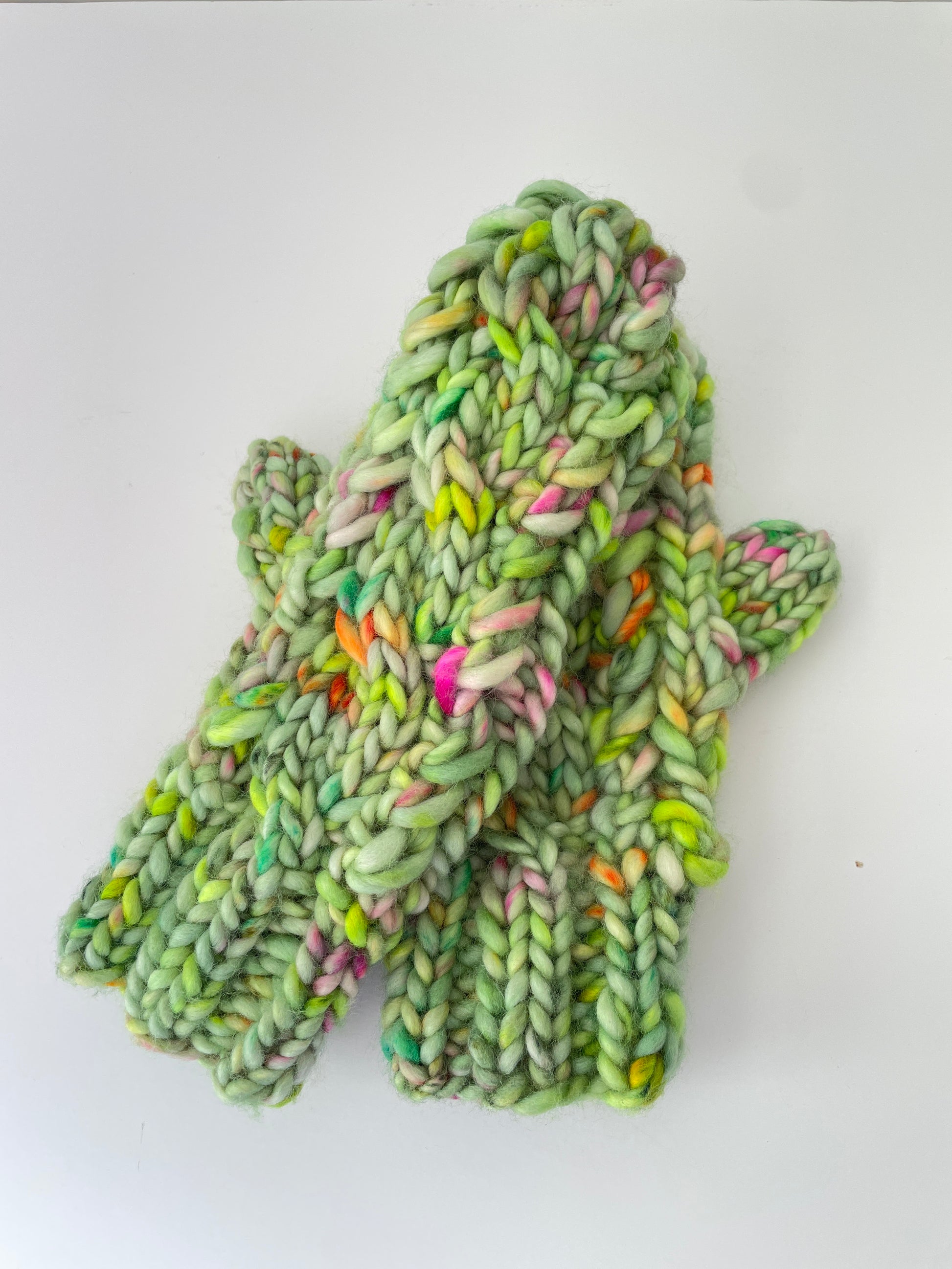 Green knitted mitts with colourful yarn on a white background