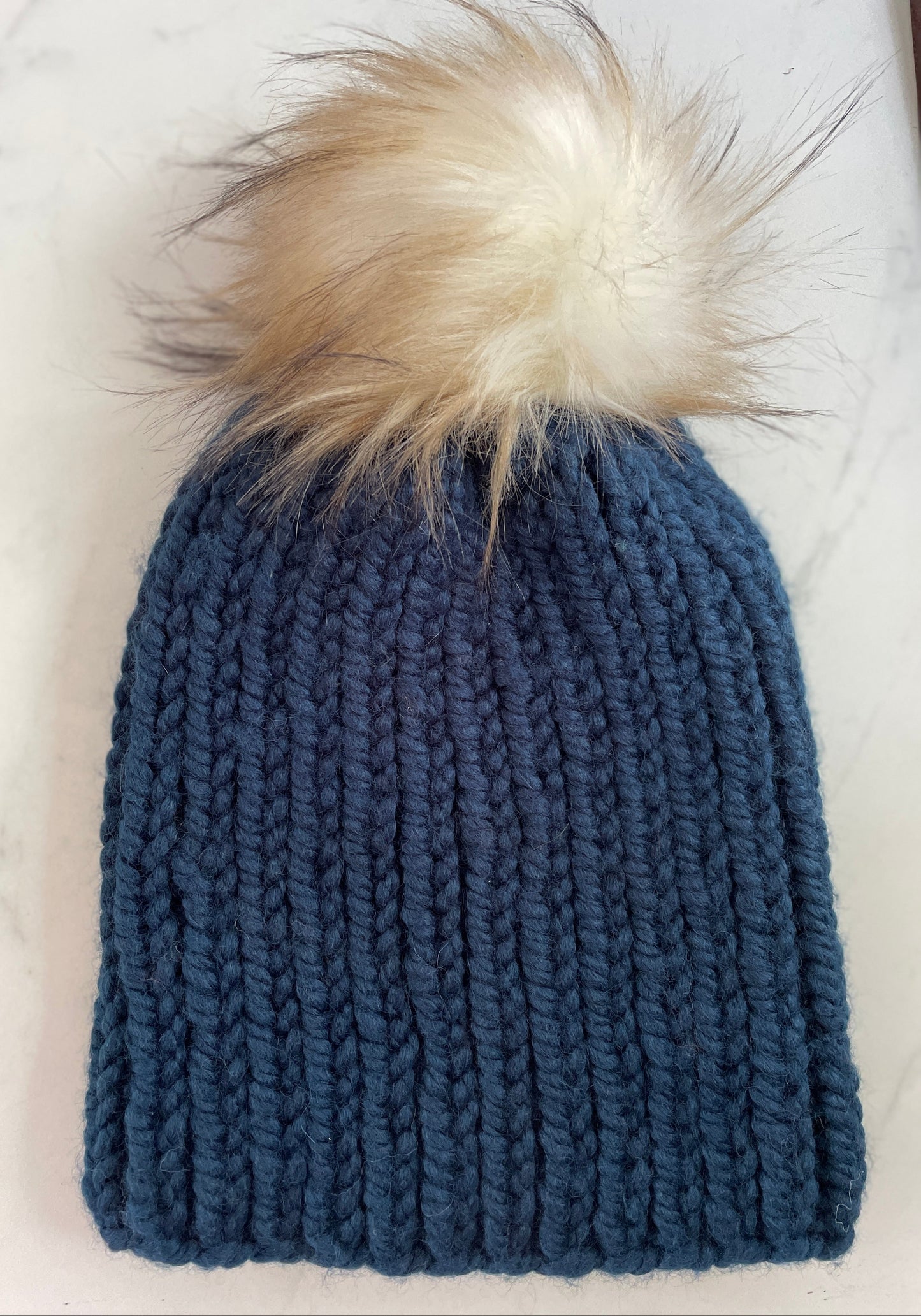 Blue knit beanie with a fur pom-pom on a white surface