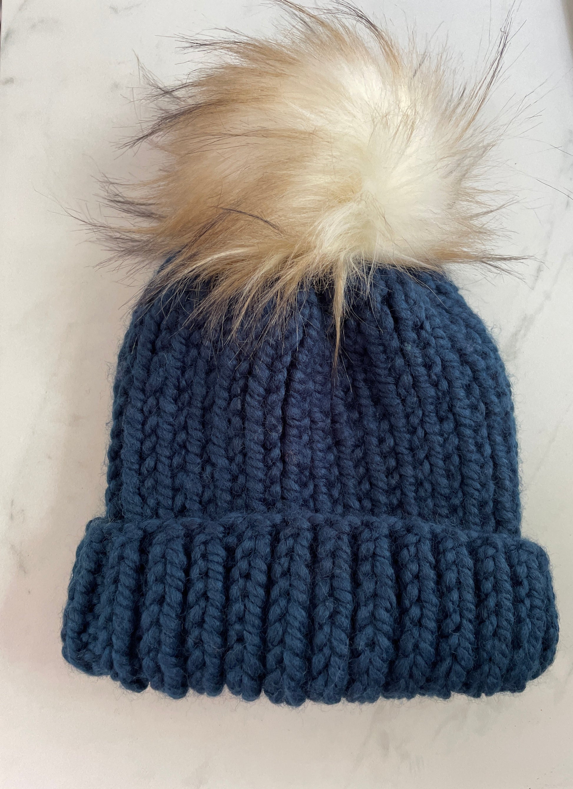 Blue knitted beanie with a fur pom-pom on a white surface