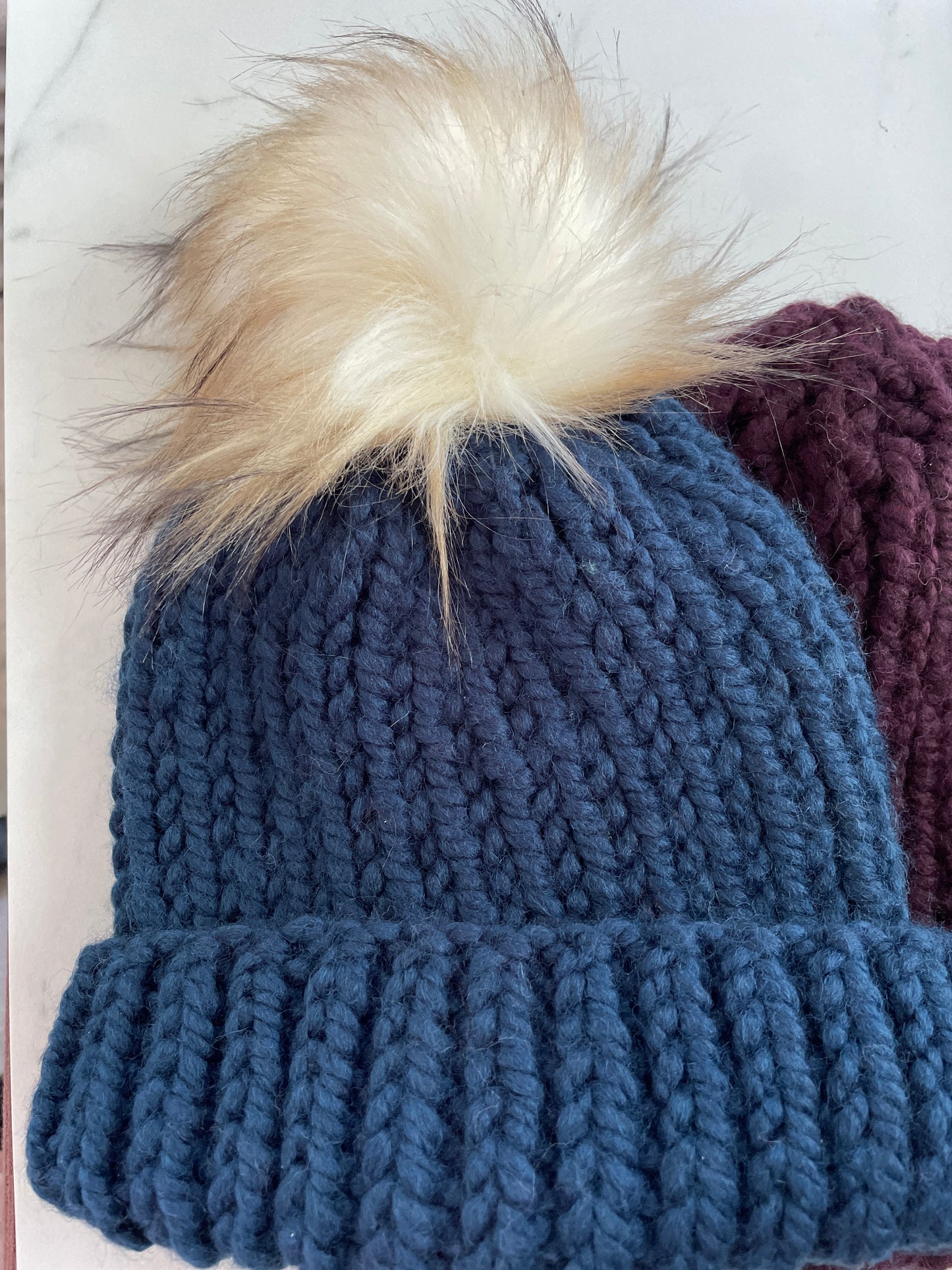 Blue knitted beanie with a fur pom-pom on a white background