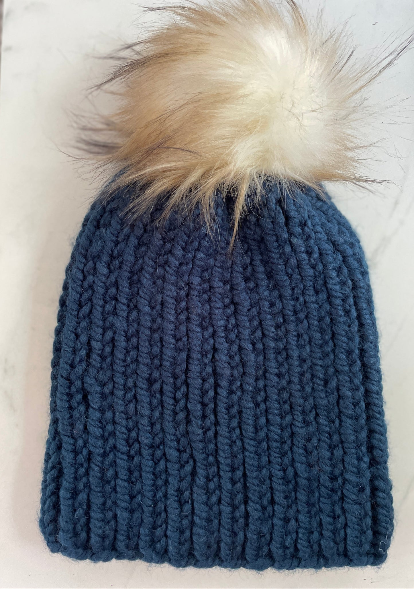 Blue knitted beanie with a fur pom-pom on a white surface