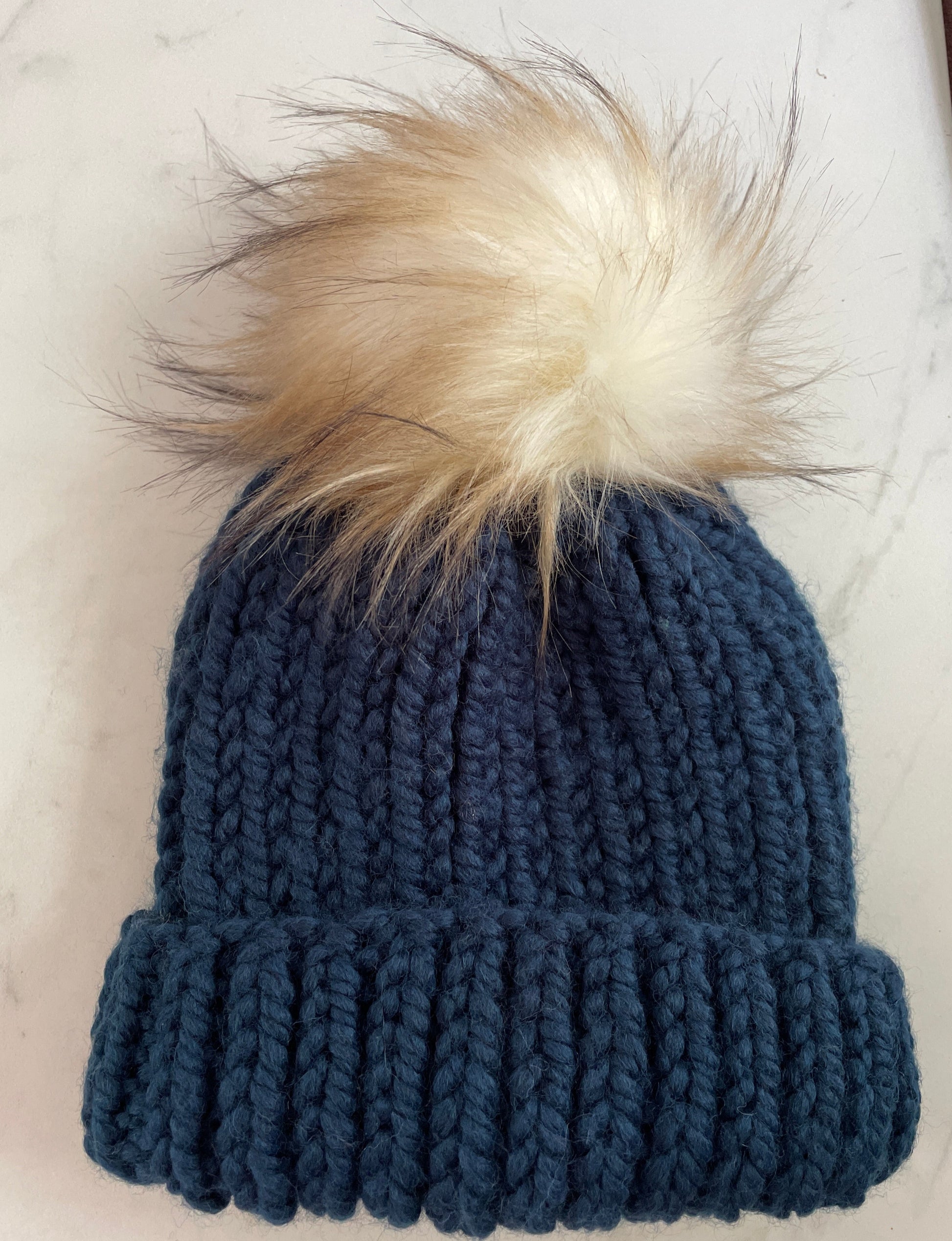 Blue knitted beanie with a fur pom-pom on a marble surface