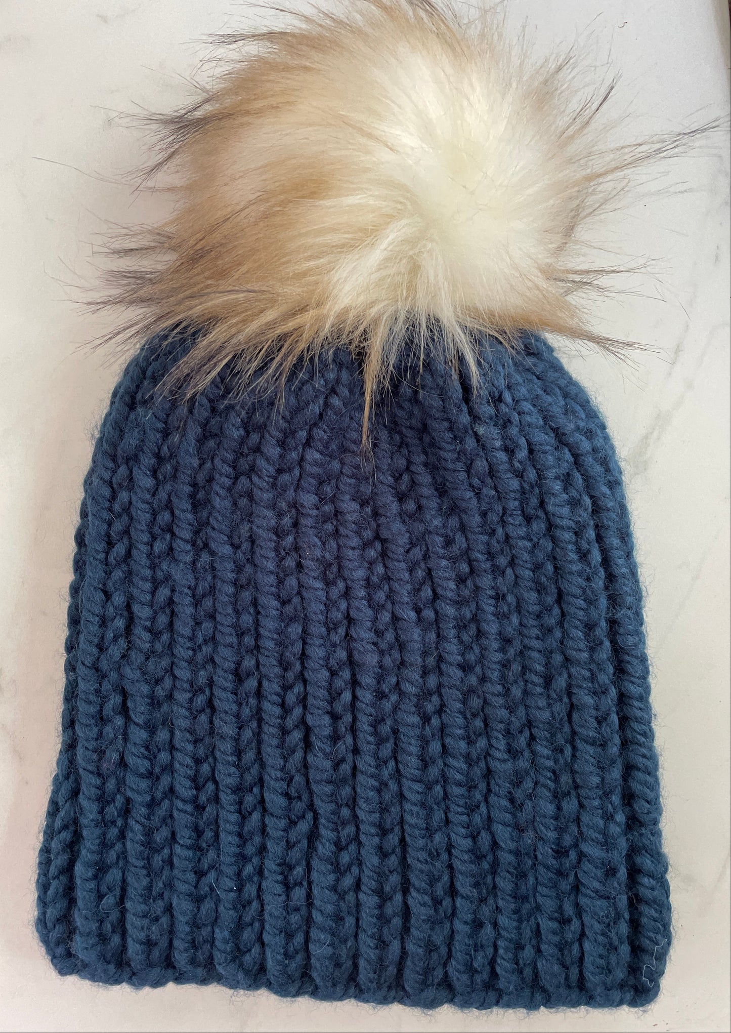 Blue knitted beanie with a fur pom-pom on a white surface