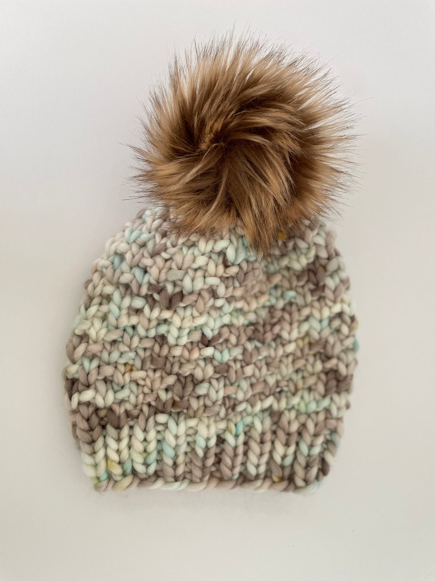 Knitted beanie with a fur pom-pom on a light background