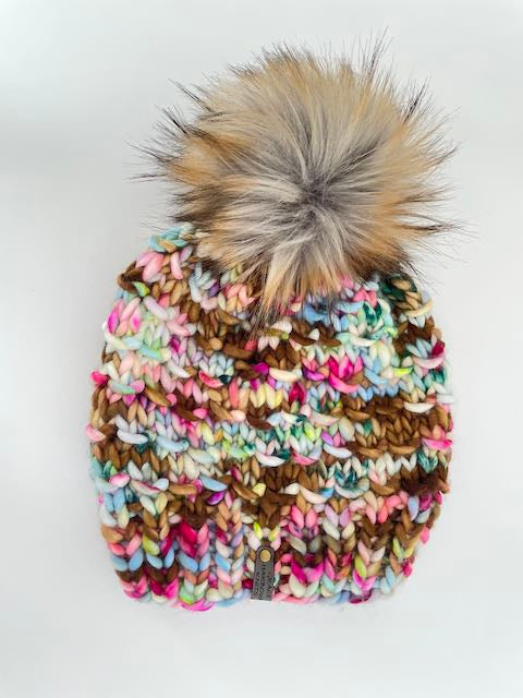 Multicolored knit beanie with a large fur pom-pom on a white background