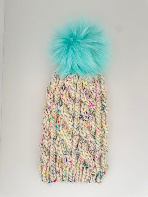 Colorful knitted beanie with a turquoise pom-pom on a light gray background